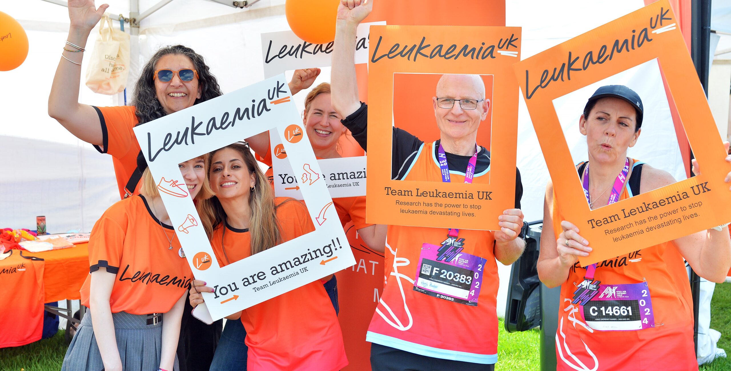 Group of 6 runners all wearing orange Leukaemia UK running vests and holding up Leukaemia UK cardboard frames
