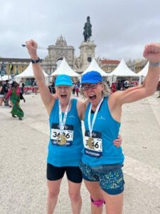 Anna and Paula in blue running tops cheering outside in Lisbon with medals around their neck