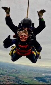 Gill mid-skydive smiling and giving two thumbs up
