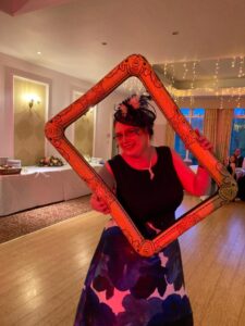 Marion McIntosh in purple and black dress, holding up and looking through a picture frame