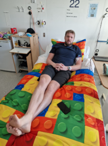 Iain laying on a hospital bed with colourful 'lego' style sheets around the time of his diagnosis