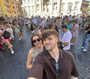 Brenda and Boyfriend MacKenzie taking a selfie in a busy, sunny square