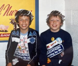 Young Braithe and Lyndon in 1985 sat smiling at the camera with paper hats on