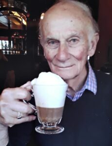 Raymond holding a hot drink with a lot of foam