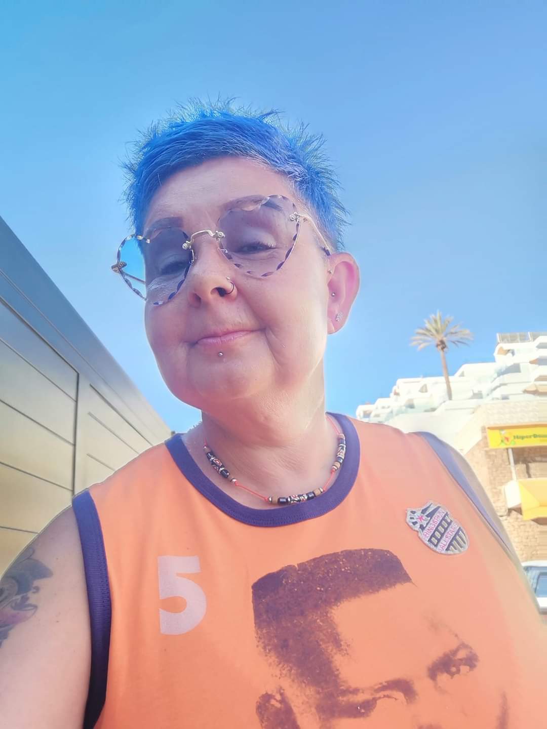 Tammy outside on a sunny day after treatment, wearing an orange top with short blue hair and glasses