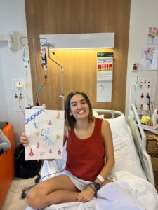 Alice in hospital holding up some arts and crafts saying 'we can do this'