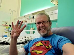 Andi in hospital holding up '4' on his fingers to represent his 4th round of Chemo