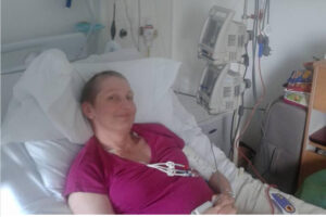 Jude in a hospital bed with short hair and pink top.