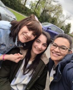 Ash outside on a street with 2 others either side of her - all smiling at the camera.