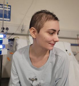 Ash with short hair sat on the hospital bed looking to her left.